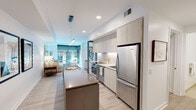 Located at 3900 Wisconsin Ave NW in Washington, DC, this thoughtfully designed single-floor residence offers a clean, contemporary aesthetic throughout. The open-concept layout connects the kitchen and living area seamlessly, creating an airy and functional living environment. Light-toned hardwood flooring runs throughout the main living spaces, enhancing the sense of openness.

The kitchen is a standout feature, equipped with flat-front cabinetry extending to the ceiling, white quartz countertops, stainless steel appliances including a Whirlpool refrigerator and electric range, a built-in dishwasher, and a generous center island with a warm taupe countertop. Pendant lighting and under-cabinet illumination add both style and functionality.

The living area is bright and welcoming, benefiting from floor-to-ceiling windows that invite natural light and offer views of the surrounding neighborhood. The bedroom is calm and understated, with neutral white walls and light wood flooring.

Two well-appointed bathrooms complete the space. The primary bathroom features large-format tile flooring, a floating wood vanity with a white basin sink, an illuminated mirror, and a glass-enclosed shower. The secondary bathroom offers a similarly minimalist design with a white vessel sink vanity and clean finishes throughout. The overall ambiance is modern, cohesive, and refined.