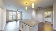 This well-designed single-floor residence offers a contemporary open-concept layout that seamlessly connects the living, dining, and kitchen areas. Rich hardwood-style flooring runs throughout the main living spaces, complemented by neutral-toned walls that create a bright, welcoming ambiance. The living area features a ceiling fan and is filled with natural light from large windows and a glass-panel entry door that frames outdoor views.

The kitchen is a standout feature, showcasing white shaker-style cabinetry, a subway tile backsplash, sleek quartz countertops, and a full suite of stainless steel appliances. A central island with pendant lighting above provides additional prep space and serves as a natural gathering point. Track lighting adds further illumination to the kitchen and adjoining areas.

The bedrooms are carpeted for comfort, each offering a ceiling fan and generous closet space, including a walk-in closet. One bedroom includes a private en-suite bathroom, while the bathrooms throughout feature large-format tile, soaking tubs with built-in wall niches, and clean, modern fixtures.

The overall aesthetic is cohesive and understated, with a neutral palette, clean lines, and thoughtful finishes that give the space a move-in-ready, contemporary feel.