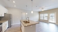 Located in Chester, Virginia, this single-story, one-bedroom, one-bathroom unit offers a thoughtfully designed open-concept layout that maximizes its compact footprint. The combined kitchen and living area serves as the heart of the home, where wood-style flooring flows throughout and neutral wall tones create a bright, cohesive atmosphere. A ceiling fan anchors the living space, which receives natural light through a window and offers access to an outdoor area via a glass-paneled door.

The kitchen is well-equipped with white shaker cabinetry, granite countertops, and a full suite of stainless steel appliances including a refrigerator, range, and over-the-range microwave. A central island with a double-basin sink and pendant lighting above adds both functionality and visual interest.

The bedroom is a comfortable size, finished with plush carpet, a ceiling fan, and a window that brings in natural light. A dedicated closet provides convenient storage. The hallway connects the main living areas to the bathroom, which features a granite-topped vanity, a full tub-shower combination, and consistent wood-style flooring, completing this clean and modern unit.