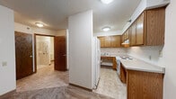 Located at 101 Riverside Dr SE in Saint Cloud, Minnesota, this one-bedroom, one-bathroom unit offers a practical and efficiently arranged single-floor layout. The combined kitchen and living room area forms the heart of the space, with the kitchen featuring warm oak cabinetry, light countertops, white appliances including a refrigerator and electric range, and tile flooring. The living area transitions seamlessly from the kitchen, highlighted by a window that frames views of lush surrounding trees and allows natural light to fill the room. Carpet flooring runs throughout the living and bedroom areas, adding warmth underfoot. The bedroom is a comfortably sized, carpeted room with its own window and baseboard heating, providing a quiet and functional retreat. The bathroom is designed with accessibility in mind, featuring a spacious roll-in tile shower equipped with grab bars, a comfort-height toilet, additional grab bar support, and easy-to-navigate tile flooring. Textured ceilings are consistent throughout the unit. The overall layout is straightforward and functional, making it a practical living space in a natural riverside setting.