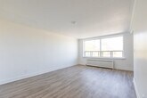 Located at 2701 Eglinton Ave in Toronto's Mount Dennis neighbourhood, this studio unit offers a clean, modern layout across a single floor. The open living area is finished with light-toned laminate hardwood flooring throughout, crisp white walls, and a textured ceiling, creating a bright and airy atmosphere. A large sliding window floods the space with natural light and frames a pleasant treetop and cityscape view, complemented by a classic radiator beneath for efficient heating. The open-concept layout connects the living area to a compact kitchen nook equipped with a stainless steel refrigerator and white cabinetry, maximizing the functionality of the space. Ample built-in closet storage is provided, along with a dedicated entry area with a double-door closet. The bathroom is thoughtfully renovated, featuring full-height white subway tile surrounding a soaker tub with a shower, chrome fixtures, a white vanity with sink, and a large mirror, delivering a clean, contemporary finish. The unit's neutral palette and well-considered layout make it a versatile and functional living space in a well-connected Toronto location.
