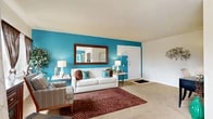 This well-organized single-floor residence offers three bedrooms and one bathroom across a compact but efficiently arranged floor plan. The living room serves as a visual centerpiece, featuring a bold teal accent wall, carpet flooring, and multiple windows that admit generous natural light. A large wall mirror enhances the sense of space in this room.

The combined dining room and kitchen area is positioned adjacent to the living room, with the dining space benefiting from a full-width sliding glass door that opens to a private balcony overlooking a residential neighborhood. The kitchen features rich dark wood cabinetry, stone-look countertops, tile flooring, and includes in-unit washer and dryer appliances conveniently integrated into the layout.

The primary bedroom is a well-proportioned retreat with a large window providing outdoor views, carpet flooring, and two closet doors. Additional bedrooms are carpeted and versatile, suitable for sleeping or office use. The single bathroom includes a wood vanity, stone-look countertop, tile flooring, and a round mirror. A hallway and dedicated closet complete the functional layout of this residence.