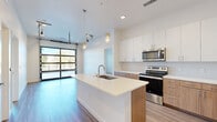 Located on W 13th Ave in Lakewood, Colorado, this contemporary 2-bedroom, 2-bathroom residence offers a thoughtfully designed single-floor layout with modern finishes throughout. The open-concept kitchen serves as the heart of the home, anchored by a generous center island with a white quartz countertop and an undermount sink. Upper white cabinetry pairs with warm wood-toned lower cabinets, complemented by stainless steel appliances including a range, microwave, and refrigerator. Stylish pendant lighting and a striking floor-to-ceiling, industrial-style garage door window flood the space with natural light and add a distinctive architectural character. Wood-look flooring runs through the main living areas, adding warmth and continuity. Both bedrooms feature plush carpeting and are well-proportioned, with the primary bedroom offering direct access to an en-suite bathroom. The primary bath includes a long vanity with warm wood cabinetry, quartz countertops, and a glass-enclosed shower. The second bathroom features a clean tiled tub-shower combination. Each bedroom is served by a closet with built-in wire shelving. A dedicated in-unit laundry room with side-by-side washer and dryer adds everyday convenience, rounding out this well-appointed Lakewood residence.