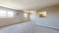 This single-floor residence offers a well-organized layout designed for comfortable everyday living. The generous living area is finished with plush wall-to-wall carpeting and neutral gray walls, creating a calm and versatile environment. Multiple windows allow natural light to fill the space, while baseboard heating and wall-mounted air conditioning units ensure year-round climate control. A pass-through opening connects the living area to the kitchen, which is outfitted with stainless steel appliances including a gas range, over-the-range microwave, and refrigerator. The kitchen features crisp white upper cabinetry, light blue lower cabinetry, a classic subway tile backsplash, stone-look countertops, and a stainless steel sink — a clean and functional cooking space. The bedrooms are carpeted and offer a similarly neutral palette, with one room featuring a built-in closet with bifold doors for practical storage. Each bedroom benefits from natural light through standard windows with blinds. The bathroom includes a full soaking tub with white tiled surround, finished in a clean, minimalist style. Overall, the residence presents a straightforward, move-in-ready layout with consistent finishes throughout.