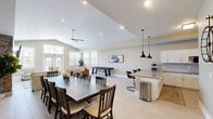 Located at 332 Brookhill Dr in Athens, Alabama, this single-floor community space offers an open-concept design that seamlessly integrates a kitchen, dining room, and living area. The layout promotes a natural flow between functional and social zones, making it well-suited for gatherings of various sizes.

The kitchen is outfitted with white shaker cabinetry, subway tile backsplash, stainless steel appliances, and a generous wraparound countertop that doubles as a breakfast bar with seating for several. A pair of dark industrial-style pendant lights hang above the bar, adding a stylish contrast to the bright, clean cabinetry.

The dining area accommodates a large dark wood table with ample seating, positioned beneath a tray ceiling with recessed lighting. Adjacent to the dining space, the living room features soaring vaulted ceilings, a ceiling fan, and a striking stacked-stone fireplace with a mounted television. Large windows and glass double doors flood the area with natural light and provide views of the outdoors.

Light-toned tile flooring runs throughout, unifying the space visually. A shuffleboard table adds a recreational element to the living area. The overall ambiance is warm, modern, and welcoming, with neutral tones and thoughtful design details throughout.