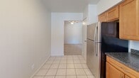 Located at 1239 Washington St in Whitehall, PA, this two-bedroom, one-bathroom unit offers a practical and comfortable single-floor layout. The kitchen is well-appointed with warm honey-toned wood cabinetry, dark granite-style countertops, tile flooring, and stainless steel appliances including a range, dishwasher, and refrigerator. A window with blinds provides natural light, and ample cabinet storage makes the space highly functional. The kitchen connects seamlessly to the living area, which features plush carpeting, a ceiling fan, and generous wall space adaptable to a variety of furniture arrangements. The expansive primary bedroom is notably spacious, offering soft carpet flooring, a large double-door closet, and a window that brings in natural light. The second bedroom is also carpeted and bright with clean, neutral walls. The bathroom includes a full tub-shower combination. A hallway connects the main areas efficiently. Outside, a private balcony overlooks well-maintained green lawns, mature trees, and a parking area, adding a pleasant outdoor dimension to the unit. The overall aesthetic is clean and neutral throughout, providing a versatile canvas for personalization.