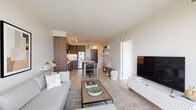 This thoughtfully designed single-floor residence showcases a contemporary aesthetic defined by clean lines, neutral tones, and light wide-plank flooring throughout. The open-concept layout connects the living, dining, and kitchen areas seamlessly, creating an inviting and functional flow. The living room features generous natural light and offers views through large floor-to-ceiling windows, with ample space for comfortable seating arrangements centered around a stylish media console.

The kitchen is well-equipped with stained wood cabinetry extending to ceiling height, stainless steel appliances including a gas range, built-in microwave, and french door refrigerator, complemented by a white subway tile backsplash and light quartz countertops. A kitchen island provides additional prep and dining space, while pendant lighting adds a refined touch.

The bedrooms are bright and spacious, each benefiting from expansive floor-to-ceiling windows that frame panoramic outdoor views. The bathroom is clean and modern, featuring a tub-shower combination, floating vanity with quartz countertop, and light tile flooring. In-unit laundry is also present. Overall, the space exudes a calm, contemporary ambiance suited for comfortable everyday living.