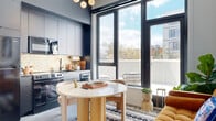 Located at 1111 Fairfield Avenue in Cleveland's vibrant Ohio City neighborhood, this thoughtfully designed one-bedroom, one-bathroom residence makes exceptional use of its compact footprint. The open-concept living and kitchen area is anchored by floor-to-ceiling black-framed windows that flood the space with natural light and offer outdoor views, complemented by a statement globe chandelier overhead. The kitchen features navy cabinetry, a decorative tile backsplash, and stainless steel appliances, flowing seamlessly into a dining nook and a cozy living area with light grey walls. A welcoming hallway with polished concrete floors and curated décor connects the living area to the private bedroom. The spacious bedroom serves as the centerpiece of the unit, showcasing a bold, art-deco-inspired botanical wallpaper accent wall, an interior pass-through window into the kitchen, and warm brass lighting details. The bathroom is finished with floor-to-ceiling vertical white tile in a walk-in glass shower, a deep forest green accent wall, and black matte fixtures, lending a sophisticated and modern aesthetic. Throughout, polished concrete flooring and crisp white walls unify the design, creating a cohesive, stylish, and highly functional living environment.