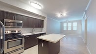 This single-floor residence offers a thoughtfully designed open-concept layout that seamlessly connects the kitchen and living area. The kitchen is a standout feature, showcasing rich dark espresso cabinetry with sleek bar-pull hardware, a light-toned countertop, and a classic subway tile backsplash. A central island provides additional prep space and serves as a natural focal point between the kitchen and the main living area. Stainless steel appliances — including a French door refrigerator with ice dispenser, range, microwave, and dishwasher — complete the kitchen's modern, functional aesthetic. Light beige large-format tile flooring runs throughout the main living and kitchen areas, contributing to a clean and cohesive look. The open living space benefits from natural light streaming through multiple windows dressed with horizontal blinds, and is finished with crown molding and a ceiling fan. A corridor leads to the bathroom, which features matching dark cabinetry, a white countertop, tile flooring set on the diagonal, and a full tub-shower combination with white tile surround. The bedroom is a spacious, light-filled room with tile flooring, crown molding, a ceiling fan, and a bank of windows that allow ample natural light to fill the space.