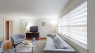 Located at Raritan Crossing, Building 1, Unit 22, this single-floor residence offers a well-organized layout with distinct living, dining, sleeping, and bathing spaces. The living room is bright and inviting, featuring large windows dressed with layered sheer blinds that allow ample natural light, warm hardwood parquet flooring, and a neutral color palette that creates a calm, contemporary atmosphere. A dedicated dining area adjacent to the kitchen accommodates a bistro-style table and seating, accented by decorative wall art. The kitchen is equipped with abundant warm-toned wooden cabinetry, granite-style countertops, a dishwasher, and a window overlooking the exterior. Two bedrooms are finished in soft blue tones, each with hardwood parquet flooring and windows that bring in natural light. The primary bedroom is spacious enough to comfortably fit a king-sized bed, while the second bedroom offers a cozy, versatile space. Two full bathrooms are tiled in classic neutral tones, each featuring a shower-tub combination with chrome fixtures and a mirrored vanity. Overall, the residence presents a clean, functional, and comfortable living environment throughout.