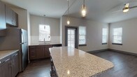 This well-designed single-floor residence offers a thoughtfully laid-out open-concept floor plan that seamlessly connects the kitchen, dining, and living areas. The kitchen is a standout feature, showcasing a large granite-topped island with pendant lighting overhead, rich dark wood cabinetry with sleek hardware, a full suite of stainless steel appliances including a range, microwave, and refrigerator, and a classic white tile backsplash. Dark hardwood-style flooring runs throughout the main living areas, adding warmth and visual continuity.

The living area is open and airy, benefiting from multiple windows fitted with blinds that allow for natural light throughout the day. Ceiling fans are present in multiple rooms, providing both comfort and functionality.

The bedrooms offer a quieter retreat, each carpeted in neutral tones and equipped with ceiling fans and windows that bring in natural light. The rooms provide generous proportions suitable for a variety of furnishing arrangements.

Two bathrooms serve the unit, each finished with granite-topped dark wood vanities, undermount sinks, brushed nickel fixtures, and large framed mirrors. One bathroom includes a full soaking tub and shower combination with white tile surround. The consistent use of granite and dark cabinetry throughout ties the design together with a cohesive, modern aesthetic.