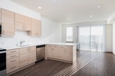 Located at 2124 W Meeker St in Kent, Washington, this single-story space is designed with a modern, minimalist aesthetic that emphasizes clean lines, neutral tones, and natural light. The interior layout flows logically from room to room, with wood-look plank flooring running consistently throughout, lending warmth and visual continuity to the space.

The kitchen is a standout feature, outfitted with flat-front light wood cabinetry that extends to the upper walls for generous storage. White quartz-style countertops provide ample workspace, complemented by a white subway tile backsplash and stainless steel appliances, including a refrigerator, electric range, over-the-range microwave, and dishwasher. A window allows natural light to brighten the space during the day.

The hallway is well-organized and functional, lined with paneled doors trimmed in warm wood tones and equipped with a wall-mounted thermostat for climate control. The corridor leads to a bright living area featuring large windows with vertical blinds that filter abundant natural light.

The bedroom area offers closet access through paneled doors, and the bathroom includes a wide vanity with a white undermount sink, quartz countertop, light wood cabinetry, a full tub and shower, and a large mirror that enhances the sense of space. Overall, the unit presents a cohesive, move-in ready environment with thoughtful, contemporary finishes.