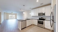 This single-floor residence offers a thoughtfully designed open-concept layout across two bedrooms, two bathrooms, and multiple dedicated spaces including closets and a laundry area. The kitchen serves as a central highlight, featuring white shaker-style cabinetry, dark granite countertops, a subway tile backsplash, and a full suite of stainless steel appliances including a range, microwave, and dishwasher. Pendant lighting over the peninsula adds a polished touch, while the space flows seamlessly into the combined kitchen and living area, which is bathed in natural light from large windows and a sliding glass door. Light wood-look flooring and a ceiling fan with integrated lighting complete the living space's clean, airy aesthetic. The bedrooms are carpeted for comfort and feature neutral tones, natural light from window views, and access to well-sized walk-in closets outfitted with wire shelving systems for organized storage. The bathrooms are finished with tile flooring, white vanities with quartz-style countertops, and glass-enclosed walk-in showers. A stacked washer and dryer unit is conveniently housed in a dedicated in-unit laundry space. Overall, the residence presents a clean, modern, and functional interior well-suited for comfortable everyday living.