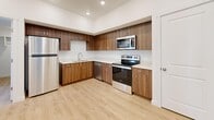 This single-floor residence offers a clean, contemporary design throughout, unified by light wood luxury vinyl flooring and crisp white walls that create a bright, airy atmosphere. The open kitchen is a standout feature, equipped with rich walnut-toned cabinetry, white quartz countertops, and a full suite of stainless steel appliances including a refrigerator, electric range, microwave, and dishwasher, all illuminated by recessed lighting above. The living areas are well-proportioned and filled with natural light, with one room featuring glass French doors that open to an outdoor view, complemented by a ceiling fan overhead. Additional rooms offer generous space, with one featuring a large window that draws in ample daylight and another ceiling fan for comfort. Bedrooms include built-in closets with paneled double doors, providing practical storage solutions. The bathrooms are finished consistently with the rest of the home, each featuring a full soaking tub and shower combination, with one bathroom also including a vanity with matching walnut cabinetry and quartz countertop. Throughout the residence, clean lines, neutral tones, and consistent finishes create a cohesive, move-in-ready environment well-suited for modern living.