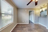 This efficiently designed one-bedroom, one-bathroom single-floor residence makes smart use of its compact footprint. The combined living, dining, and kitchen area forms the heart of the unit, featuring rich dark hardwood-style flooring that runs throughout the space. Crown molding and crisp white baseboards add a polished finish, while a ceiling fan with a light fixture provides both comfort and illumination. A window fitted with horizontal blinds allows natural light to brighten the open living area, creating an airy feel. The kitchen is equipped with white cabinetry, a granite-patterned countertop with an integrated sink, and a full-size refrigerator, offering functional storage and prep space. The bedroom is a comfortable, well-proportioned room with the same hardwood-style flooring and textured walls in a neutral taupe tone, complemented by a closet with classic six-panel doors for added storage. The full bathroom features a white tub and shower combo unit, a toilet, and a white vanity, all finished with consistent wood-look flooring. Neutral wall tones throughout the unit create a cohesive, move-in-ready aesthetic well-suited for efficient, comfortable everyday living.