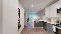 Located at 215 E State St in downtown Ithaca, NY, this one-bedroom, one-bathroom unit offers a well-designed layout across a single floor. The open-concept kitchen and living area serves as the heart of the unit, where the kitchen features two-tone cabinetry—white uppers paired with slate gray lowers—topped with crisp white quartz countertops. A peninsula provides casual seating and additional prep space, while stainless steel appliances, including a full-size refrigerator, range, microwave, and dishwasher, complete the setup. Sleek pendant lights hang above the peninsula, adding a modern touch. The living area receives natural light through a large window fitted with horizontal blinds, creating a bright and comfortable atmosphere. Warm-toned hardwood-style flooring flows consistently throughout the unit, lending a cohesive and contemporary feel. The bedroom is a cozy, well-proportioned space featuring its own large window that fills the room with natural light. The bathroom includes a glass-enclosed walk-in shower with white subway tile walls. A dedicated entry area with coat hooks and a closet provides practical storage. The overall aesthetic is clean, modern, and efficiently designed.