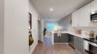 Located at 215 E State St in downtown Ithaca, NY, this one-bedroom, one-bathroom unit offers a well-designed layout across a single floor. The open-concept kitchen and living area serves as the heart of the unit, where the kitchen features two-tone cabinetry—white uppers paired with slate gray lowers—topped with crisp white quartz countertops. A peninsula provides casual seating and additional prep space, while stainless steel appliances, including a full-size refrigerator, range, microwave, and dishwasher, complete the setup. Sleek pendant lights hang above the peninsula, adding a modern touch. The living area receives natural light through a large window fitted with horizontal blinds, creating a bright and comfortable atmosphere. Warm-toned hardwood-style flooring flows consistently throughout the unit, lending a cohesive and contemporary feel. The bedroom is a cozy, well-proportioned space featuring its own large window that fills the room with natural light. The bathroom includes a glass-enclosed walk-in shower with white subway tile walls. A dedicated entry area with coat hooks and a closet provides practical storage. The overall aesthetic is clean, modern, and efficiently designed.