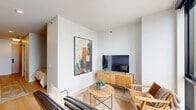 Located on a high floor at 1475 N Kingsbury St in Chicago's vibrant Lincoln Park/Goose Island corridor, Unit 2409 is a thoughtfully designed studio that maximizes every square foot with a clean, contemporary aesthetic. The living area is the undeniable centerpiece of the space, anchored by expansive floor-to-ceiling windows that flood the room with natural light and frame impressive panoramic views of the Chicago skyline and surrounding cityscape. Light hardwood flooring runs throughout, complementing the neutral white walls and creating a warm, airy atmosphere. The open layout accommodates a defined sleeping nook, separated by a partial wall partition that offers a sense of privacy without sacrificing the open feel of the space. The bathroom is finished in a modern, minimalist style, featuring large-format light tile flooring, a sleek wood-toned vanity with ample storage cabinetry, a white countertop, and a combined tub and shower. The overall design of the unit reflects a cohesive modern sensibility — clean lines, natural wood accents, and a restrained neutral palette — making it a polished and efficient high-rise retreat in the heart of Chicago.