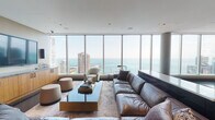 Located in the heart of Chicago's Streeterville neighborhood, this elegant high-rise space at 340 E North Water Street delivers a commanding presence through its seamless blend of contemporary architecture and premium finishes. Expansive floor-to-ceiling windows wrap the living area, flooding the space with natural light while framing breathtaking panoramic views of Lake Michigan, the Chicago River, and the city skyline.

The open-concept living area is anchored by a generously scaled sectional sofa, a glass-and-brass coffee table, and a large wall-mounted display, all set against a backdrop of warm neutral tones and rich wood cabinetry. Floating shelves add a refined decorative touch, while recessed ceiling lighting and in-ceiling speakers enhance the polished ambiance throughout.

The kitchen is a standout feature, showcasing a substantial island topped with dramatic veined marble-style stone countertops and natural bamboo cabinetry. A stainless steel overhead range hood serves as an architectural centerpiece, complemented by a bold blue tile backsplash, professional-grade appliances, and dark stone tile flooring. Pendant lighting over the dining area adds warmth, while the surrounding floor-to-ceiling glass ensures the kitchen remains connected to the sweeping lakefront views. The overall design is cohesive, sophisticated, and tailored for both everyday living and refined entertaining.