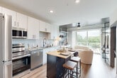 Located at 555 Boulevard NE in Atlanta's vibrant Old Fourth Ward neighborhood, this one-bedroom, one-bathroom unit offers a well-designed open-concept layout across a single floor. The kitchen is a standout feature, outfitted with a full suite of stainless steel appliances — including a refrigerator, electric range, built-in microwave, and dishwasher — complemented by crisp white cabinetry, a subtle tile backsplash, and light wood-tone flooring. A dark-framed island with a butcher block top provides additional prep space and casual seating. The living area flows seamlessly from the kitchen toward expansive sliding glass doors that open to a private balcony, flooding the space with natural light and offering pleasant views of the surrounding tree canopy. The bedroom is a comfortable retreat featuring a large window with outdoor views, warm neutral tones, and soft carpeting underfoot. The bathroom is finished in a clean, contemporary style with light stone-look tile flooring, a grey-topped vanity, and matte black hardware accents throughout. Recessed lighting, a ceiling fan, and wood-look flooring tie the common areas together for a cohesive, modern aesthetic throughout the unit.