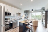 Located at 555 Boulevard NE in Atlanta's vibrant Old Fourth Ward neighborhood, this one-bedroom, one-bathroom unit offers a well-designed open-concept layout across a single floor. The kitchen is a standout feature, outfitted with a full suite of stainless steel appliances — including a refrigerator, electric range, built-in microwave, and dishwasher — complemented by crisp white cabinetry, a subtle tile backsplash, and light wood-tone flooring. A dark-framed island with a butcher block top provides additional prep space and casual seating. The living area flows seamlessly from the kitchen toward expansive sliding glass doors that open to a private balcony, flooding the space with natural light and offering pleasant views of the surrounding tree canopy. The bedroom is a comfortable retreat featuring a large window with outdoor views, warm neutral tones, and soft carpeting underfoot. The bathroom is finished in a clean, contemporary style with light stone-look tile flooring, a grey-topped vanity, and matte black hardware accents throughout. Recessed lighting, a ceiling fan, and wood-look flooring tie the common areas together for a cohesive, modern aesthetic throughout the unit.