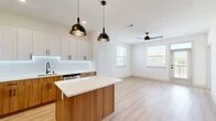 Located at 5300 Las Soleras Dr in Santa Fe, New Mexico, this thoughtfully designed one-bedroom, one-bathroom residence offers a clean, contemporary aesthetic throughout its single-floor layout. Light wood-style flooring flows through the main living areas, complemented by crisp white walls and an abundance of natural light from multiple windows.

The open-concept kitchen and living room serves as the heart of the home. The kitchen is well-appointed with two-tone cabinetry — warm wood lower cabinets paired with white upper cabinets — stainless steel appliances including a gas range, microwave, and refrigerator, a white quartz countertop, tile backsplash, matte black fixtures, and a central island with pendant lighting overhead. The living area features a ceiling fan and direct access to a private patio with outdoor views.

The bedroom is carpeted for comfort, receives natural light through a window framing scenic New Mexico landscape views, and includes a dedicated closet accessed through a stylish sliding barn door. The bathroom features wood-tone cabinetry, a white quartz vanity, an LED-lit mirror, matte black hardware, and a sleek frameless glass sliding shower enclosure. Additional conveniences include an in-unit laundry area and a hallway connecting all spaces efficiently.