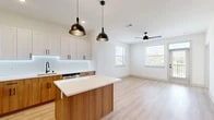 Located at 5300 Las Soleras Dr in Santa Fe, New Mexico, this thoughtfully designed one-bedroom, one-bathroom residence offers a clean, contemporary aesthetic throughout its single-floor layout. Light wood-style flooring flows through the main living areas, complemented by crisp white walls and an abundance of natural light from multiple windows.

The open-concept kitchen and living room serves as the heart of the home. The kitchen is well-appointed with two-tone cabinetry — warm wood lower cabinets paired with white upper cabinets — stainless steel appliances including a gas range, microwave, and refrigerator, a white quartz countertop, tile backsplash, matte black fixtures, and a central island with pendant lighting overhead. The living area features a ceiling fan and direct access to a private patio with outdoor views.

The bedroom is carpeted for comfort, receives natural light through a window framing scenic New Mexico landscape views, and includes a dedicated closet accessed through a stylish sliding barn door. The bathroom features wood-tone cabinetry, a white quartz vanity, an LED-lit mirror, matte black hardware, and a sleek frameless glass sliding shower enclosure. Additional conveniences include an in-unit laundry area and a hallway connecting all spaces efficiently.