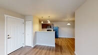 Located in Airway Heights, Washington, this single-floor unit at 11103 W Sixth Ave offers a thoughtfully designed open-concept layout finished with warm wood-look flooring throughout the main living areas. The kitchen is a standout feature, equipped with rich dark cabinetry, stone-look countertops, stainless and black appliances including a refrigerator, electric range, and built-in microwave. A peninsula with pendant lighting above creates a natural divide between the kitchen and the open living space, ideal for casual dining or entertaining. The living area is bright and airy, benefiting from a sliding glass door that opens to a private balcony with views of the surrounding community. The bedrooms are carpeted for comfort, each offering closet storage. The unit includes two bathrooms—one featuring a soaking tub with shower combination and the other with a dedicated shower, both finished with light neutral tones and wood-look flooring. A dedicated in-unit laundry room accommodates a full-size washer and dryer with additional shelving for storage. The overall palette of warm beige tones, clean white trim, and consistent flooring creates a cohesive and functional living environment throughout.