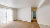 This single-floor residential unit offers a clean, functional layout with a neutral color palette and consistent finishes throughout. The living area is generously sized, featuring warm beige carpeting, crisp white walls, and a sliding glass door fitted with vertical blinds that allows natural light to fill the space. A hallway connects the living area to the rest of the unit, leading to the private rooms and bathroom.

The galley-style kitchen is efficiently designed, featuring light-toned cabinetry with wood trim accents, a white electric coil range, a full-size refrigerator, a built-in dishwasher, and a single-basin sink. Light ceramic tile flooring runs throughout the kitchen, providing a clean and practical surface.

The bedrooms are carpeted and finished with white walls, each offering windows with blinds that bring in natural light. The rooms provide a comfortable, functional space with ample wall area for furniture placement.

The bathroom is straightforward and well-maintained, featuring tile flooring, a full tub-shower combination, a toilet, and a vanity with storage. The overall layout of the unit is practical and open, with each area clearly defined while maintaining a cohesive, understated aesthetic throughout.