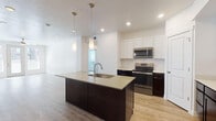 This single-floor residence offers a well-designed, open-concept layout with a clean, contemporary aesthetic throughout. The kitchen serves as a central highlight, featuring a large island with an integrated sink and light quartz-style countertops, dark espresso cabinetry below contrasted by white upper cabinets, and a white subway tile backsplash. Stainless steel appliances, including a refrigerator, range, and built-in microwave, complete the functional cooking space. Pendant lighting above the island adds a refined touch. Light wood-look flooring flows through the kitchen and living areas, enhancing the bright, airy feel created by recessed lighting and natural light from multiple windows.

The living area is spacious and open, equipped with a ceiling fan and access to a private balcony through a glass-paneled door. Bedrooms feature plush carpet flooring, ceiling fans, and windows that allow natural light. One bedroom includes wood-look flooring and direct balcony access.

Two bathrooms maintain the consistent design language with dark vanity cabinetry, light countertops, and large mirrors. The primary bathroom includes an extended vanity with ample storage, while the second bathroom offers a tub-shower combination. Generous closet space is visible throughout the unit.