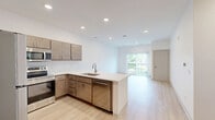 Located at 4965 Plainfield Ave NE in Grand Rapids, Michigan, this thoughtfully designed 2-bedroom, 1-bathroom unit offers a clean, modern aesthetic throughout its efficiently laid-out single floor. Light wood luxury vinyl flooring flows seamlessly through every room, complementing the crisp white walls and creating a bright, cohesive atmosphere.

The open-concept kitchen and living area forms the heart of the unit. The kitchen is outfitted with stainless steel appliances — including a refrigerator, range, and microwave — warm-toned wood cabinetry, a white quartz countertop, a subway tile backsplash, and a peninsula with an undermount sink that opens to the living space. Recessed lighting illuminates the area, which also features a sliding glass door leading to a private balcony overlooking lush green outdoor views.

Both bedrooms are generously proportioned, with the primary bedroom offering multiple windows that fill the space with natural light. Each bedroom includes sliding panel closet doors for convenient storage. The shared full bathroom features a combination tub and shower, a wood-tone vanity with a white countertop, and light flooring that maintains the unit's modern, clean design language throughout.