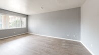 Located at 1015 Cardenas Dr SE in Albuquerque, New Mexico, this single-story, one-bedroom, one-bathroom home offers a well-designed, efficient layout. Light gray walls and warm-toned luxury vinyl plank flooring run consistently throughout, creating a cohesive and clean aesthetic. The spacious living room features a textured ceiling and large windows dressed with vertical blinds, allowing ample natural light to fill the space. A built-in wall heater unit provides practical comfort. The combined dining and kitchen area is configured as a galley-style kitchen, featuring white cabinetry with warm wood trim accents, a white countertop with an integrated sink, and white appliances including a refrigerator and range. A window at the end of the kitchen brings in additional natural light. The generously sized bedroom includes a ceiling fan with light fixture, a wide window with vertical blinds, and multiple closets — including a built-in vanity nook — offering excellent storage. The bathroom is a standout feature, showcasing floor-to-ceiling marble-look tile surrounding the soaking tub and shower, complemented by a white vanity with a single sink and a high window for ventilation. A connecting hallway and three total closets complete this smartly organized home.