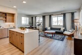 Located along the iconic Pacific Coast Highway in Dana Point, this single-floor coastal residence offers a thoughtfully designed open-concept layout filled with natural light and contemporary finishes throughout. The living area is anchored by wide-plank hardwood flooring, recessed lighting, and large windows dressed with elegant drape panels, framing views of the surrounding coastal community. A tufted sofa, gold-accented shelving, and a decorative area rug create a sophisticated yet relaxed atmosphere. The kitchen is a standout, featuring warm wood cabinetry, a crisp white tile backsplash, stainless steel appliances including a Bosch range, a black matte faucet, and an expansive quartz island that flows seamlessly into the living space. A dedicated dining area with abundant window light offers an inviting setting for meals. The primary bedroom features a bold geometric accent wall, plush carpeting, a walk-in closet, and direct access to a well-appointed en suite bathroom complete with a dual-sink floating vanity, warm wood cabinetry, a full-width mirror with backlit lighting, and a frameless glass walk-in shower. Additional windows throughout the space invite Southern California sunshine, enhancing the bright, airy ambiance of this refined coastal home.