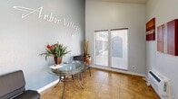 Located at 8028 S Central Ave in Phoenix, Arizona, this single-floor leasing office serves as the welcoming face of Arbor Village. The space is thoughtfully designed to create a professional yet inviting atmosphere for prospective and current residents alike.

The interior features warm earth-toned tile flooring throughout, complemented by soft blue-gray walls that lend the space a calm, approachable feel. The "Arbor Village" branded signage is prominently displayed on the main wall, reinforcing the community's identity. Vaulted ceilings rise dramatically in the windowed area, amplifying the sense of openness despite the compact footprint.

Natural light streams in generously through multiple large windows fitted with horizontal blinds, offering views of the surrounding community. A glass-topped table with decorative plants and community literature serves as a central feature of the reception area, providing an inviting place for guests to review information. Seating is available for visitors, and a dedicated office area with a workstation is visible through a connecting doorway, supporting leasing staff operations.

The space also displays fair housing compliance notices, underscoring its professional, regulatory-compliant operation. A wall-mounted climate control unit ensures comfort year-round. Overall, the office strikes a balance between functional efficiency and a welcoming residential aesthetic.