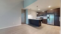 This two-floor residence showcases a thoughtfully designed open-concept layout with consistent modern finishes throughout. The main living area is anchored by dramatic vaulted ceilings and light wood-style flooring, creating an airy, expansive atmosphere. Sliding glass doors lead to a private balcony overlooking mature trees, filling the space with natural light. A ceiling fan completes this generous living area.

The kitchen is well-appointed with dark espresso cabinetry, light granite countertops, a subway tile backsplash, and a full suite of stainless steel appliances including a gas range, built-in microwave, and French door refrigerator. A large kitchen island with a built-in sink and pendant lighting serves as a functional centerpiece. Bedrooms feature tray ceilings, wood-style flooring, and large windows with outdoor views.

Two bathrooms serve the upper level — one with a tiled shower-tub combo and white cabinetry, another with a glass-enclosed walk-in shower and tile flooring. The lower level offers two generously sized bonus rooms with plush carpeting and recessed lighting, as well as closet storage, providing versatile space for various uses.