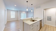This single-story residence on Blue Bonnet Drive in Brighton, Colorado offers a thoughtfully designed layout with two bedrooms and three bathrooms. The interior reflects a clean, modern aesthetic, characterized by crisp white walls, light wood-look flooring in the main living areas, and neutral carpeting in the bedrooms.

The open-concept kitchen serves as a central feature, equipped with white shaker-style cabinetry, light quartz countertops, stainless steel appliances including a refrigerator, range, microwave, and dishwasher, and a peninsula with pendant lighting overhead. The kitchen flows naturally into the living room, which features recessed lighting, a window, and a sliding glass door fitted with vertical blinds that invite natural light.

Two hallways connect the bedrooms and three bathrooms, maintaining efficient circulation throughout the unit. The bathrooms are finished with white vanities, quartz countertops, and modern light fixtures. The primary bedroom offers a comfortable, carpeted retreat with direct sightlines to the kitchen area. A dedicated laundry space and additional closet storage add practical functionality. The overall ambiance is bright, clean, and move-in ready.