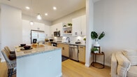 Located at 1650 Clearwater Largo Rd in Largo, Florida, this single-floor residence presents a thoughtfully designed open-concept layout with contemporary finishes and a bright, coastal-inspired aesthetic. Light wood-tone flooring flows seamlessly throughout the space, unifying each area and contributing to an airy, cohesive feel.

The kitchen serves as a central highlight, featuring granite countertops, a large island with bar seating and pendant lighting overhead, and a two-tone cabinet design pairing crisp white upper cabinets with warm natural wood lower cabinetry. Stainless steel appliances, a white subway tile backsplash, open shelving, and matte black hardware complete the polished look. The kitchen transitions effortlessly into the dining and living areas, which benefit from multiple windows and a glass door that invite natural light and outdoor views.

The living room is welcoming and relaxed, with neutral tones, ample natural light, sheer curtains, and access to the outdoors. The bedroom offers a serene retreat with generous natural light from plantation-shuttered windows and hardwood-style flooring. The bathroom is finished with granite-topped wood vanity cabinetry, a soaking tub with shower combination, and clean white tile surround. Overall, the space strikes a refined balance of modern design and comfortable Florida living.