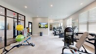 Located at 7505 Founders Way in Franklin, Indiana, this fitness center offers a well-equipped, single-floor exercise space designed to support a wide range of workout routines. The room features a clean, neutral color palette with light beige walls, a smooth white ceiling with recessed lighting, and wall-to-wall carpeting that provides a comfortable surface underfoot.

The cardio zone is lined with multiple treadmills, an elliptical trainer, and a recumbent bike, all positioned along one side of the room beneath large windows fitted with white blinds that allow natural light to filter in. Full-length mirrors are strategically placed to enhance the sense of space and provide visual feedback during workouts.

The strength training area includes a multi-station cable machine, a dedicated leg extension/curl machine, and a tiered dumbbell rack stocked with a range of free weights. A functional training station offers stability balls, resistance bands, medicine balls, and a foldable workout bench, catering to flexibility and cross-training needs.

A wall-mounted flat-screen television adds an entertainment element to the space. The room is further defined by floor-to-ceiling glass partition walls with dark steel frames, offering visual connectivity to an adjacent lounge or common area. A split-system air conditioning unit ensures climate control throughout the year, making this fitness center a practical and inviting space for daily exercise.