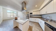 Located at 9110 W Tropicana in Las Vegas, NV, this well-appointed 1-bedroom, 1-bathroom unit offers a thoughtfully designed open-concept layout with modern finishes throughout. The kitchen is a standout feature, boasting white shaker cabinetry, dark countertops, a subway tile backsplash, and a full suite of stainless steel appliances including a gas cooktop, dishwasher, and refrigerator. A central island with a stainless steel range hood serves as the kitchen's focal point, flowing seamlessly into the combined dining and living areas. Wood-style flooring runs throughout the main living spaces, complemented by large windows that invite abundant natural light. The living room opens to a private balcony with views of the surrounding palm tree-lined landscape. The bedroom features plush carpeting, soaring ceilings, a sliding glass door to the balcony, and a dedicated walk-in closet. The full bathroom is finished with wood-look tile flooring, a quartz-style vanity countertop, and a tub-shower combination. Additional conveniences include an in-unit laundry area, a built-in storage cabinet with wine rack, and recessed lighting throughout, making this a functional and stylish Las Vegas residence.