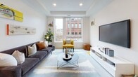 Located at 34 Munroe St in Lynn, Massachusetts, this thoughtfully designed single-floor residence offers a clean, contemporary aesthetic throughout. The open-concept living area serves as the heart of the unit, featuring recessed lighting, a tray ceiling, and large windows that frame views of the surrounding urban streetscape, flooding the space with natural light. The living room provides ample space for comfortable furnishings and flows seamlessly into the dining and kitchen areas.

The kitchen is outfitted with sleek taupe cabinetry, white quartz countertops, stainless steel appliances including a range, microwave, and refrigerator, a tile backsplash, and pendant lighting — combining both style and functionality.

The unit includes multiple bedrooms, each benefiting from large windows with urban views and neutral tones that create a calm, restful atmosphere. The primary bedroom features floor-to-ceiling corner windows that maximize natural light and city views.

Two well-appointed bathrooms feature gray vanity cabinetry, white quartz countertops, black hardware accents, backlit mirrors, and light wood-style flooring, delivering a polished, modern finish throughout. The overall design palette of whites, grays, and warm wood tones creates a cohesive and inviting living environment.
