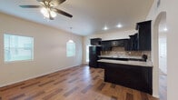 Located at 12727 Tierra Este Rd in El Paso, Texas, this single-story home offers a well-designed layout that combines functionality with modern finishes throughout. The open-concept living and dining area flows seamlessly into the kitchen, creating a welcoming communal space. Rich wood-look flooring extends across the main living areas, complemented by ceiling fans that enhance comfort and airflow.

The kitchen is a standout feature, showcasing bold dark cabinetry with raised-panel detailing, light granite countertops, and a neutral tile backsplash in a classic square mosaic pattern. Black appliances, including a range with overhead microwave and a full-size refrigerator, are integrated into the design. A peninsula provides additional prep and seating space, making the kitchen both practical and visually striking.

The bedrooms are finished with warm, neutral carpet and receive natural light through slatted blinds. Each room offers a clean, blank canvas well-suited for a variety of layouts and furnishings.

The bathroom continues the home's cohesive design with wood-look tile flooring, a dark vanity with granite countertop, a framed mirror, and a tub-shower combination. Clean white walls and bright lighting keep the space feeling fresh and functional. Arched architectural details are visible throughout, adding a subtle decorative element to the overall design.