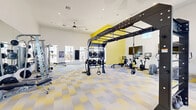 Located at 4747 N 99th Ave in Phoenix, AZ, this well-appointed fitness center offers a generous, open single-floor layout designed to accommodate a wide range of workout styles. The space is defined by striking yellow accent walls and a bold geometric-patterned floor in yellow and grey, creating an energetic and motivating atmosphere throughout.

Soaring ceilings with recessed lighting and ceiling fans ensure the space remains bright and well-ventilated. Large windows and glass-panel doors along the perimeter allow abundant natural light to flood the interior while offering views of the surrounding exterior.

The facility is comprehensively equipped for both strength and cardio training. A multi-functional overhead rig serves as a centerpiece, supporting suspension trainers and pull-up bars. Nearby, a dedicated strength zone features a multi-stack cable machine, smith machine, and weight benches accompanied by a full rack of dumbbells. Floor-to-ceiling mirrors along one wall visually expand the space and assist users during training.

A separate cardio area houses treadmills, ellipticals, upright bikes, and a rowing machine, all positioned in front of wall-mounted flat-screen televisions. Functional training accessories, including medicine balls, battle ropes, and TRX straps, round out the offerings. The overall design balances style and functionality, making this fitness center a comprehensive and inviting space for all fitness levels.