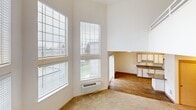 Located in Vancouver, Washington, this two-bedroom, two-bathroom residence spans two floors and offers a well-thought-out layout with an abundance of functional spaces. The main floor is the heart of the home, highlighted by a soaring two-story living room with floor-to-ceiling windows that flood the space with natural light. Warm hardwood-style flooring flows through the kitchen and dining areas, while plush carpeting adds comfort to the living and bedroom spaces. The kitchen features light wood cabinetry, ample counter space, and a sink positioned to overlook the adjacent living area. Two full bathrooms are finished with wood-toned vanity cabinetry, grey countertops, large mirrors, and wood-style flooring; one includes a full tub-shower combination. Both bedrooms are generously proportioned with soft carpeting, natural light from windows with blinds, and direct access to closets. The primary bedroom connects to its own bathroom for added convenience. A dedicated laundry area and multiple closets throughout ensure practical storage. Upstairs, a loft area overlooks the main living space, adding versatile square footage. A private balcony offers outdoor views of the surrounding neighborhood and tree line, completing this well-appointed multi-story residence.