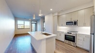 This well-designed one-bedroom, one-bathroom unit in Erie, Colorado offers a thoughtfully laid-out floor plan that maximizes every square foot. The open-concept kitchen and living area serves as the heart of the home, anchored by a sleek white kitchen island with an integrated sink and pendant lighting above. The kitchen is outfitted with stainless steel appliances — including a range, microwave, and refrigerator — complemented by light gray cabinetry, white quartz countertops, and a classic subway tile backsplash. Warm hardwood-style flooring flows throughout the main living areas, lending a cohesive and contemporary feel. The living area is bathed in natural light from large windows, with direct access to a private outdoor balcony that offers open neighborhood views. The bedroom features plush carpeting, a ceiling fan, a bright window, and its own balcony access, creating a comfortable and airy retreat. A dedicated closet provides practical built-in shelving and hanging storage. The full bathroom is elegantly finished with a dual-sink white vanity, a large framed mirror, wood-look flooring, and a tub-shower combination with floor-to-ceiling tile surround. Clean lines and a neutral palette throughout give this unit a modern, move-in-ready appeal.