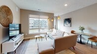 This single-floor residence offers a thoughtfully designed open-concept layout that seamlessly connects the kitchen, dining, and living areas. The kitchen is a standout feature, showcasing two-tone cabinetry with crisp white upper cabinets and dark wood lower cabinets, granite countertops, a generously sized island with bar seating for two, and a full suite of stainless steel appliances including a refrigerator, range, microwave, and dishwasher. Pendant lighting adds a modern touch above both the island and kitchen workspace. The open living area benefits from large windows that invite abundant natural light and views of the surrounding neighborhood. Wood-style flooring runs throughout the main living spaces, contributing to a warm, cohesive aesthetic. The primary bedroom is a calm retreat with soft carpeting, warm taupe walls, and ample space for furnishings. A second bedroom also features carpet, a ceiling fan, and a large window with outdoor views. The bathroom is well-equipped with a dual-sink granite vanity, dark wood cabinetry, wood-style flooring, and a tub-shower combination. In-unit laundry is visible off the bathroom, adding everyday convenience. The overall ambiance is contemporary and inviting.