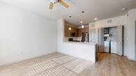This single-floor residence is designed with a clean, modern aesthetic that emphasizes open living. Light wood-tone flooring runs throughout, creating a cohesive and airy feel across all areas of the home.

The living area is bright and open, benefiting from natural light and a ceiling fan overhead. It flows seamlessly into the kitchen, which is separated by a peninsula counter with a light quartz-style surface and an integrated sink. Pendant lights hang above the peninsula, providing focused illumination. The kitchen is well-appointed with taupe shaker-style cabinetry, stainless steel appliances including a refrigerator, microwave, and range, and a classic tile backsplash. A dedicated laundry closet with a full-size washer and dryer is conveniently located just off the kitchen.

The bedroom features two windows fitted with blinds, allowing for ample natural light, along with a ceiling fan and access to additional spaces via a paneled interior door.

The bathroom is finished with a light-toned tile surround in the tub/shower combo, a single vanity with a light countertop, a framed mirror, and overhead cabinetry for additional storage, all maintaining the home's neutral, cohesive palette.