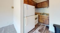 Located at 8802 Three Chopt Rd in Henrico, Virginia, this single-floor unit offers a straightforward, functional layout across several distinct spaces. The living area is a notable highlight, featuring soft carpeting underfoot and a large sliding glass door that fills the room with natural light and provides direct access to a balcony. The balcony overlooks mature, leafy trees, offering a pleasant outdoor view and a sense of privacy. A wall-mounted heating unit is positioned along the base of one wall, providing climate control to the space.

The kitchen is a compact, enclosed area equipped with warm-toned wooden cabinetry, a white refrigerator, a gas range, and a sink, all set atop wood-look plank flooring that adds a durable, practical element to the space.

The bedroom is carpeted and receives natural light through a window with an outdoor view of the surrounding greenery. A louvered closet door with built-in shelving provides organized storage. A wall-mounted air conditioning unit offers additional climate control.

The bathroom features wood-look plank flooring, a tub-shower combination with white tile surround, a single vanity with an integrated sink, and standard fixtures, completing this straightforward and functional unit.