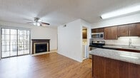 This single-story, 2-bedroom, 1-bathroom home offers a well-organized layout across a compact yet functional floor plan. The living room serves as a central gathering space, featuring warm wood-look flooring, a ceiling fan, a textured ceiling, and a classic brick-surround fireplace with a dark wood mantel. A sliding glass door allows natural light to filter into the room and provides outdoor access. The kitchen is well-appointed with rich dark wood cabinetry, stainless steel appliances including a range, microwave, and refrigerator, and a granite-topped center island that flows into the adjacent dining area. A dedicated laundry area is conveniently accessible from the kitchen and houses a full-size washer and dryer with overhead cabinetry for storage. The two bedrooms feature the same wood-look flooring, ceiling fans, and ample closet space, with the secondary bedroom offering a large window with natural light. The bathroom is finished with white tile, a tub-shower combination, a decorative mosaic tile accent border, and granite-topped vanity cabinetry. Throughout the home, white walls and consistent flooring create a clean, cohesive aesthetic.