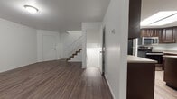 This three-floor residence is thoughtfully laid out across multiple levels, each serving a distinct purpose. The main living level features rich, dark hardwood-style flooring throughout an open and airy layout, with a staircase connecting the floors and a front entry door providing direct access. The kitchen is well-appointed with dark espresso cabinetry, stone-look countertops, stainless steel appliances including a range, microwave, and dishwasher, and a double-basin sink. A skylight above the kitchen area brings in additional natural light, enhancing the overall brightness. The kitchen flows into an open dining or living area with wood-style flooring and a window that invites natural light. The upper level hosts carpeted bedrooms, each offering a comfortable, quiet retreat with windows and closet access. The bathrooms are finished with dark wood vanities, stone-look countertops, large mirrors, vinyl plank flooring, and full tub-shower combinations. The lower level presents an unfinished basement space with concrete flooring and exposed framing, offering significant potential for customization or additional storage. Throughout the home, clean white walls and consistent finishes create a cohesive and move-in ready aesthetic.