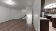 This three-floor residence is thoughtfully laid out across multiple levels, each serving a distinct purpose. The main living level features rich, dark hardwood-style flooring throughout an open and airy layout, with a staircase connecting the floors and a front entry door providing direct access. The kitchen is well-appointed with dark espresso cabinetry, stone-look countertops, stainless steel appliances including a range, microwave, and dishwasher, and a double-basin sink. A skylight above the kitchen area brings in additional natural light, enhancing the overall brightness. The kitchen flows into an open dining or living area with wood-style flooring and a window that invites natural light. The upper level hosts carpeted bedrooms, each offering a comfortable, quiet retreat with windows and closet access. The bathrooms are finished with dark wood vanities, stone-look countertops, large mirrors, vinyl plank flooring, and full tub-shower combinations. The lower level presents an unfinished basement space with concrete flooring and exposed framing, offering significant potential for customization or additional storage. Throughout the home, clean white walls and consistent finishes create a cohesive and move-in ready aesthetic.